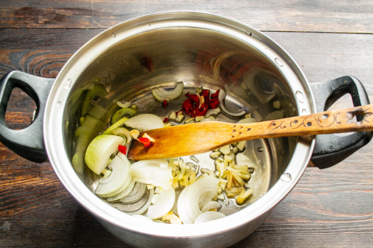 Starting the Soup Base with Freshly Chopped Vegetables Chopped onions, garlic, and chili being added to a heavy-bottomed pot with olive oil.