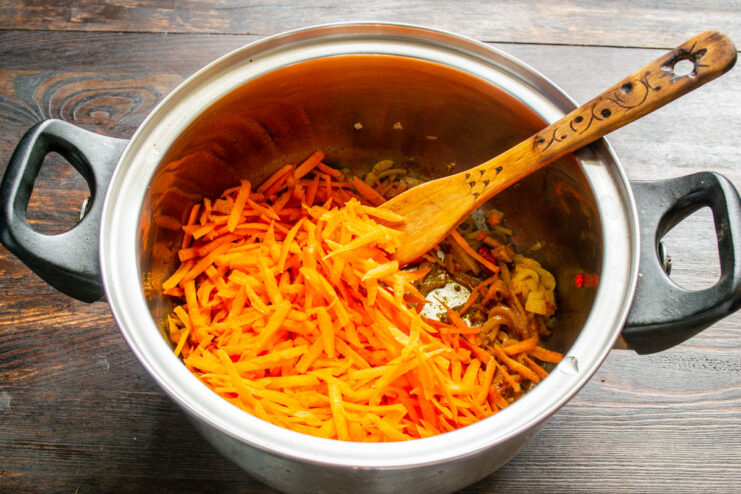 Incorporating Grated Carrots for Sweetness and Color Grated carrots being added to the pot with sautéed onions and spices.