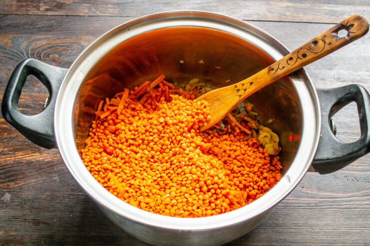 Adding Red Lentils for a Creamy Texture and Protein Dry red lentils being poured into the pot with cooked vegetables.