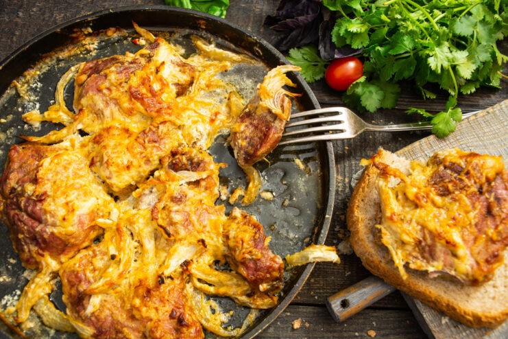 A baking dish with freshly baked Myaso po-frantsuzski, featuring a golden cheese crust and garnished with herbs.