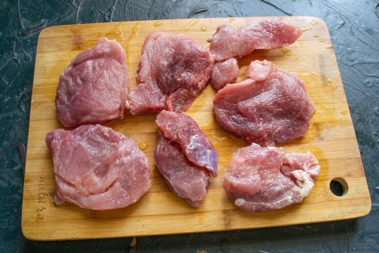 How to Properly Slice Pork for Myaso po-Frantsuzski Raw pork tenderloin being sliced into thick medallions on a wooden cutting board.