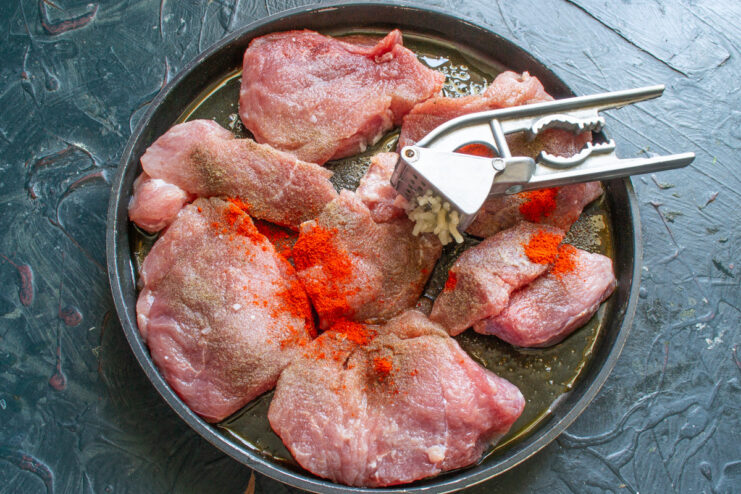 Seasoning the Pork with Paprika and Herbs Seasoning pork slices in a baking dish with paprika and dried herbs before baking.