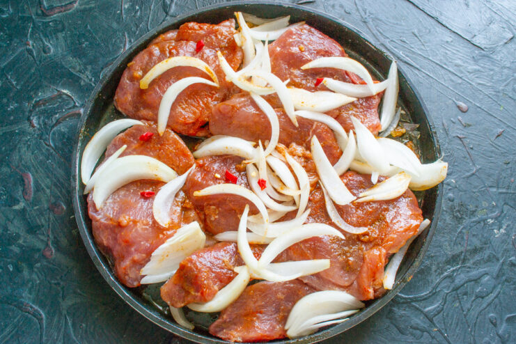Layering Onions and Chili for Extra Flavor Layers of sliced onion and chili pepper placed over seasoned pork in a baking dish.