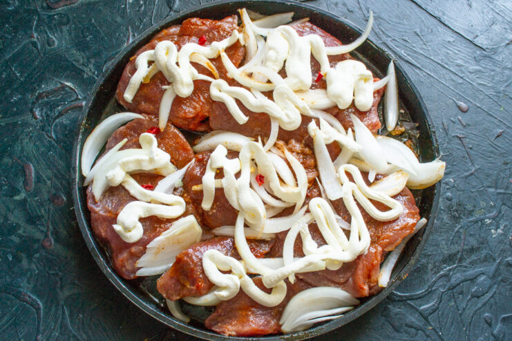 Adding a Creamy Smetana Topping A layer of thick smetana (sour cream) being spread over onions and pork in a baking dish.