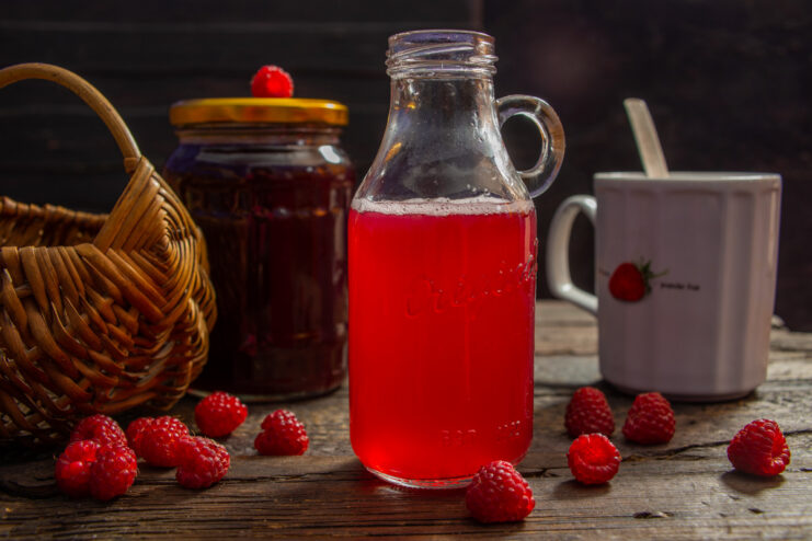 A glass bottle of homemade natural sugar-free raspberry juice, with fresh raspberries nearby.
