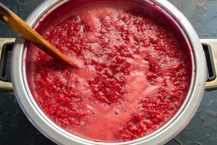 Gently Heating Raspberries to Extract Flavor A pot of raspberries and water being gently heated on the stove, with a wooden spoon for stirring.