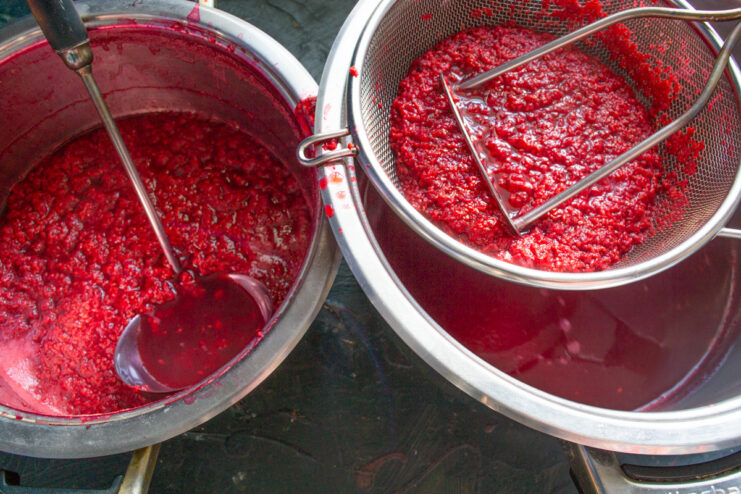 Straining the Raspberry Mixture to Get Pure Juice Pouring raspberry puree through a fine sieve lined with cheesecloth to separate the juice from solids.