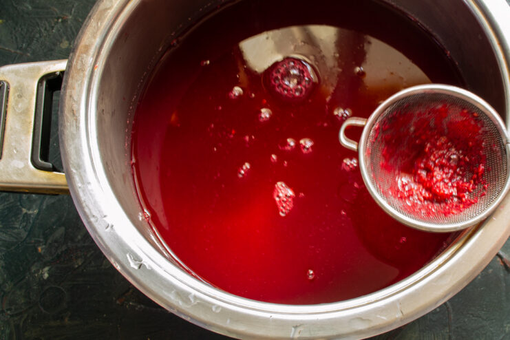 Final Filtering for a Clear Raspberry Juice Filtering raspberry juice through a fine mesh sieve into a clean bowl for a clear final product.