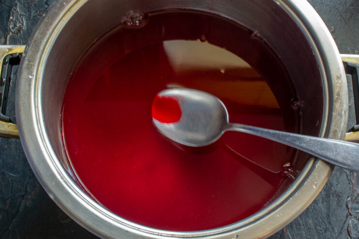 Bringing the Filtered Raspberry Juice to a Boil for Preservation A pot of clear, red raspberry juice being brought to a boil on the stove before canning.
