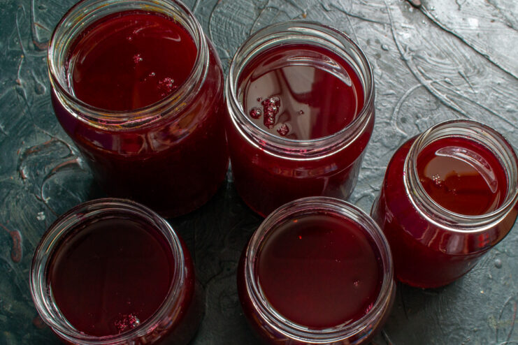 Water Bath Canning: Pasteurizing Raspberry Juice for Long-Term Storage Glass jars filled with raspberry juice submerged in a large pot of water for pasteurization.