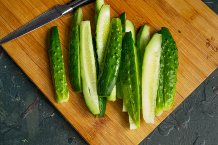 How to Prepare Cucumbers for Pickling Close-up of pickling cucumbers being sliced into long, thin strips on a cutting board.