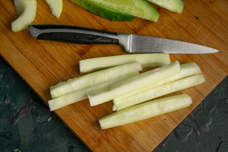 Preparing Zucchini for Pickling Strips Zucchini being cut into long, thin strips on a wooden board, matching the cucumber slices.