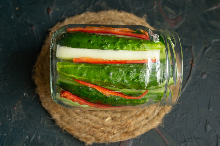 Layering Vegetables in the Jar for Pickling A glass jar being filled with alternating layers of sliced cucumber, zucchini, and red chili strips.