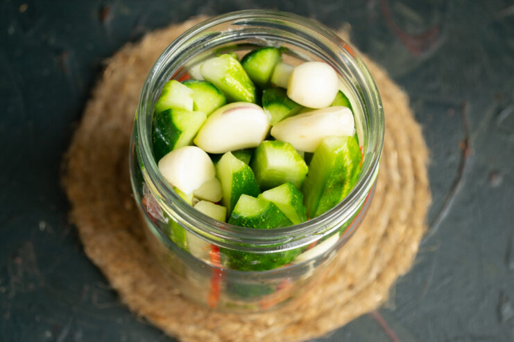 Adding Garlic for Extra Flavor in Pickles Peeled garlic cloves being added to a jar filled with sliced cucumbers and zucchini.
