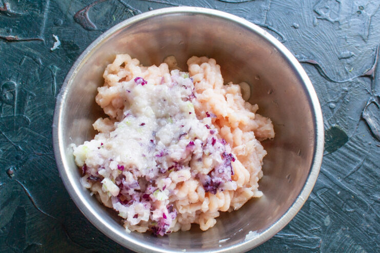 Grinding Chicken, Garlic, and Shallots Together A meat grinder processing chicken fillet, garlic, and shallots into a bowl.