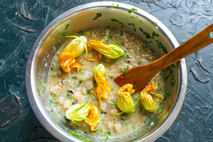 Incorporating Zucchini Flowers into the Omelette Mix Adding chopped zucchini flowers to the omelette batter in a bowl.