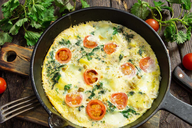 A finished nettle and potato omelet in a pan, topped with mozzarella and cherry tomatoes.