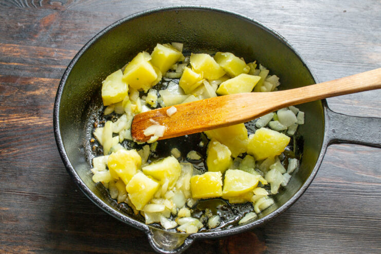 Frying Potatoes and Onions for the Omelet Base Diced boiled potatoes being fried with sautéed onions in a pan.