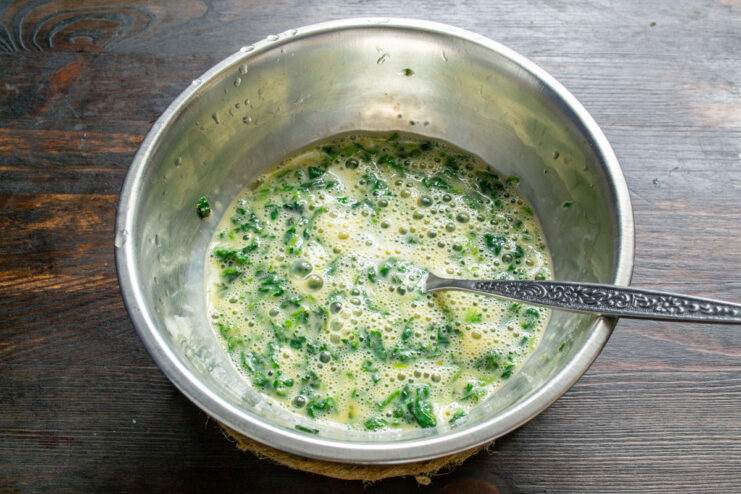 Combining Eggs and Nettles for a Flavorful Omelet Whisking eggs and chopped nettles together in a bowl with a fork.