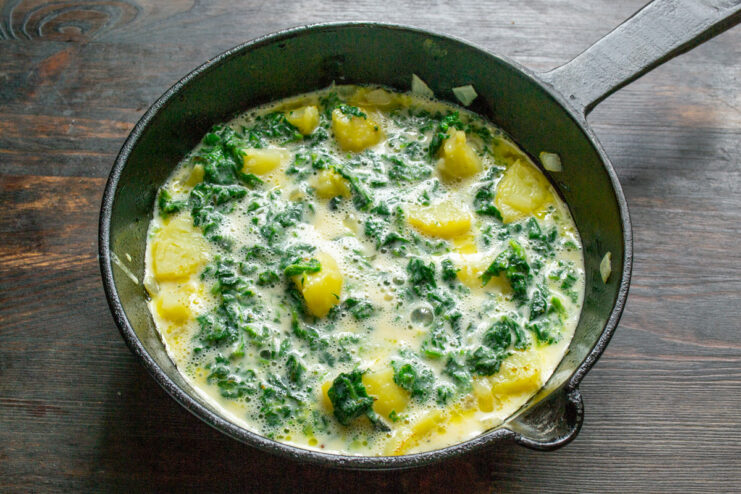 Adding the Egg Mixture to the Pan Pouring the egg and nettle mixture into a pan with fried potatoes and onions.