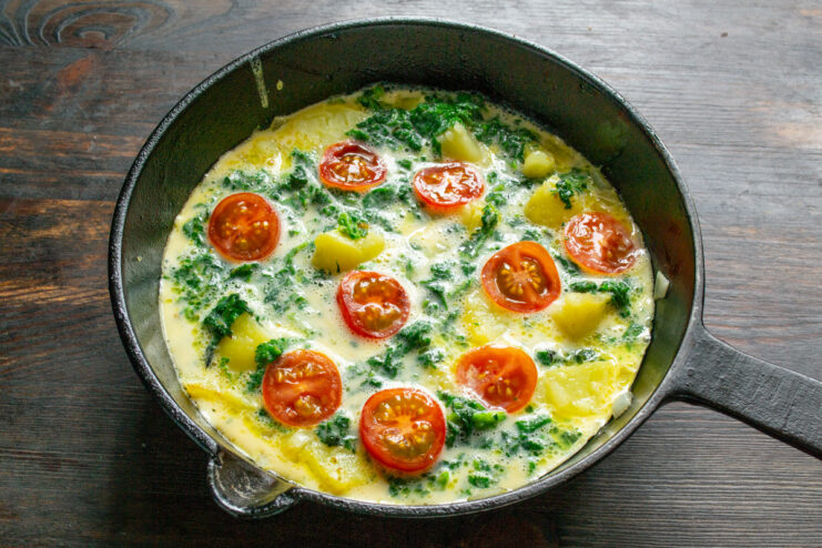 Topping the Omelet with Fresh Cherry Tomatoes Halved cherry tomatoes being arranged on top of the uncooked omelet in the pan.