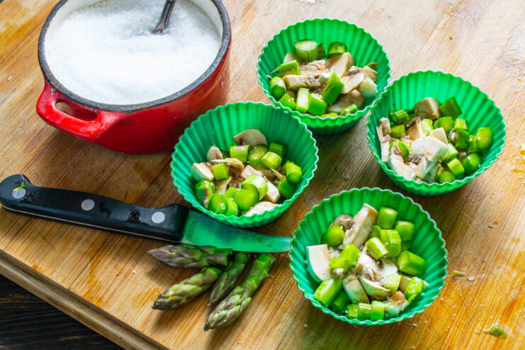 Layering Vegetables in Silicone Molds for the Omelette Chopped asparagus and mushrooms placed in silicone muffin molds.