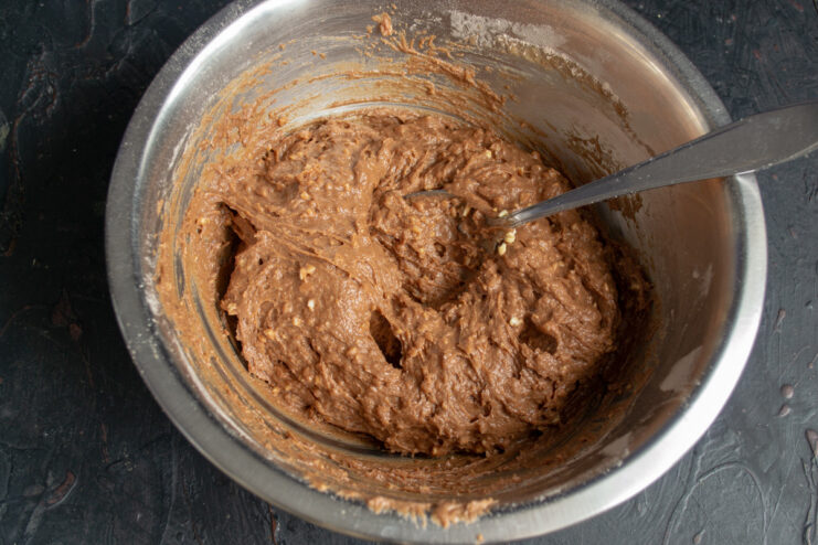 Folding the chopped nuts into the final cake batter. Folding chopped toasted almonds into the chocolate cake batter in a bowl.