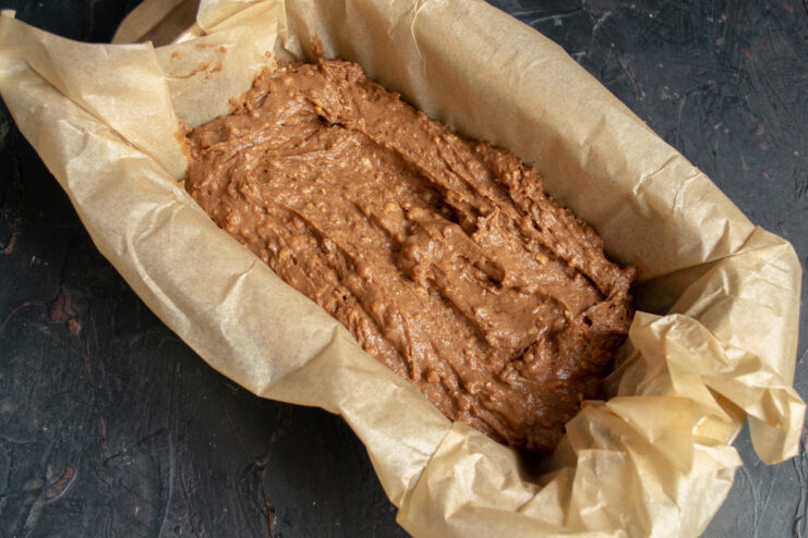Spreading the batter evenly in a parchment-lined loaf pan. Pouring the finished nut and cocoa cake batter into a parchment-lined loaf pan.