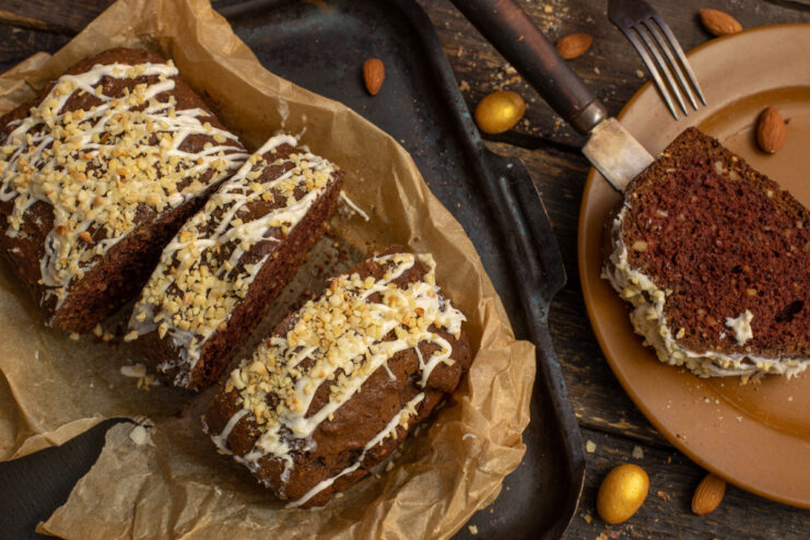 A slice of nut cake with cocoa on a plate, drizzled with white chocolate and topped with chopped nuts.