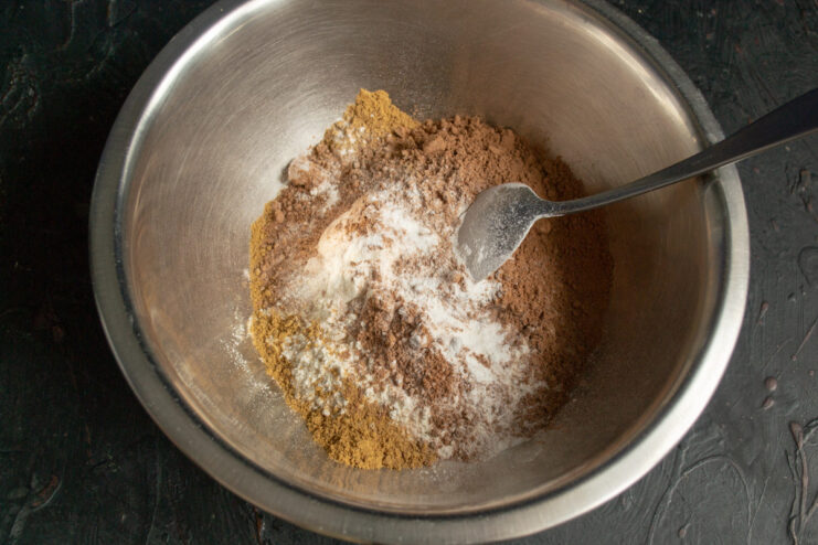 Whisking dry ingredients ensures an even bake. A bowl containing dry ingredients like flour, cocoa powder, and spices, being mixed.