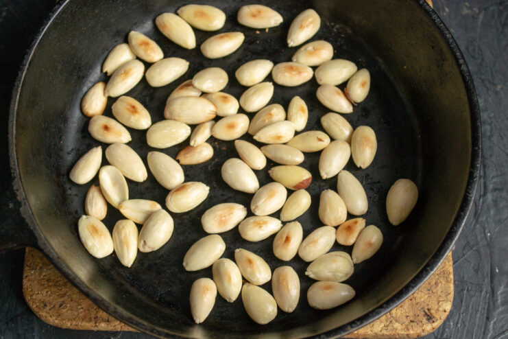 Toasting almonds in a skillet to enhance their flavor. Blanched almonds being toasted in a cast-iron skillet.