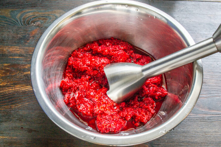 Step 1: Blending fresh raspberries into a smooth puree. An immersion blender pureeing fresh raspberries in a white bowl.