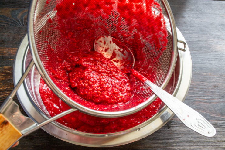 The result: smooth, seedless raspberry puree. A bowl of smooth, seedless raspberry puree next to the leftover seeds in a sieve.