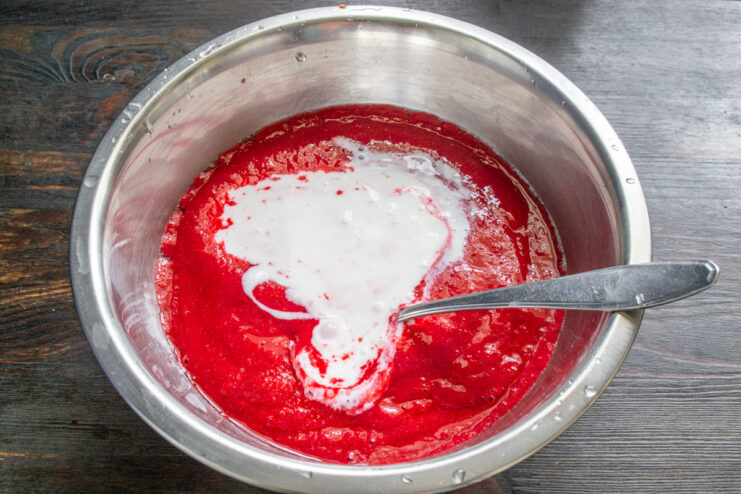 Step 4: Adding cold kefir to the sweetened raspberry puree. Pouring white kefir from a glass bottle into the bowl with raspberry puree.