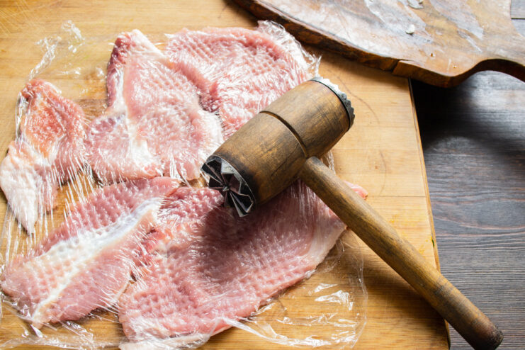 Using a Meat Mallet to Tenderize Pork Cutlets Pork cutlets covered with plastic wrap being tenderized with a meat mallet.