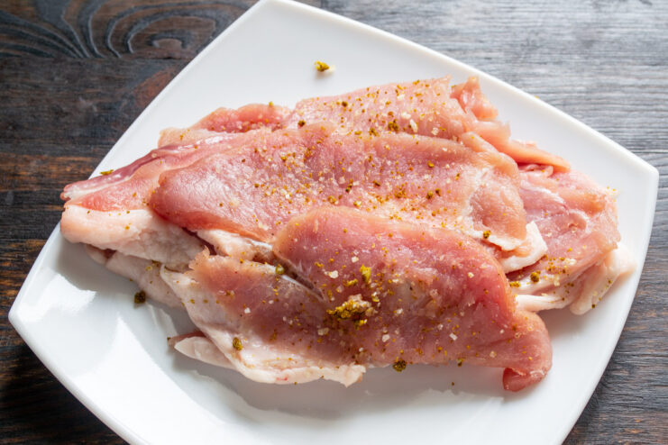 Letting the Seasoned Pork Marinate Before Cooking Thin, seasoned pork cutlets stacked on a plate to marinate.