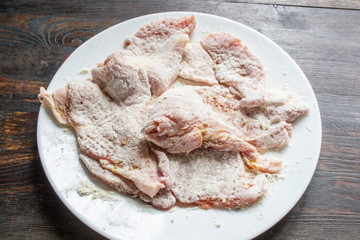 Dredging the Pork Chops in Flour for an Even Coating A thin pork cutlet being lightly coated in all-purpose flour.