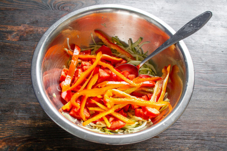 A hand slicing a red bell pepper into thin strips on a cutting board.