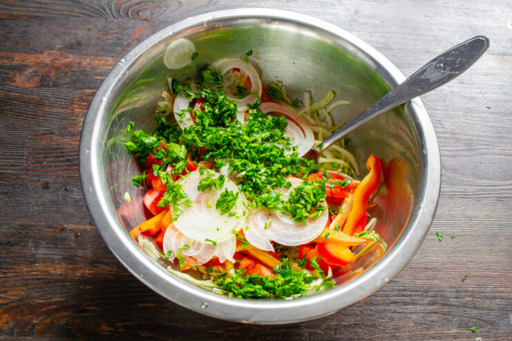 Sliced onions and chopped parsley being added to the bowl of vegetables.