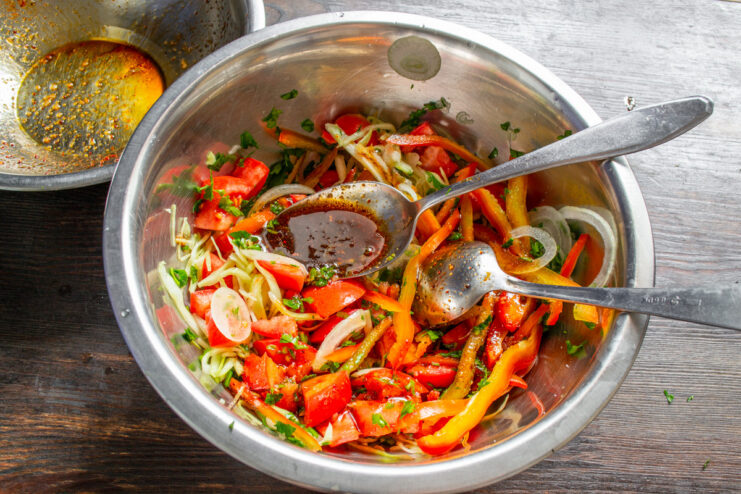 Pouring the prepared honey dressing over the mixed vegetable salad in a bowl.