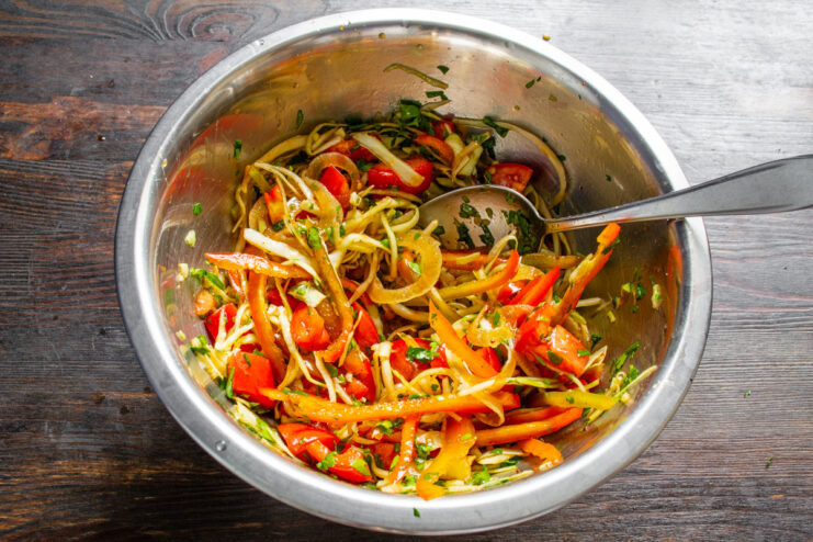 Tossing the vegetable salad with two spoons to mix it with the honey dressing.
