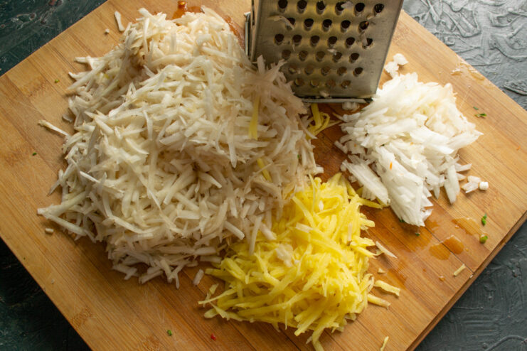 Grating Jerusalem artichokes and potatoes for the vegetable patties. A food processor can also be used. The process of grating Jerusalem artichokes and potatoes using a coarse vegetable grater.