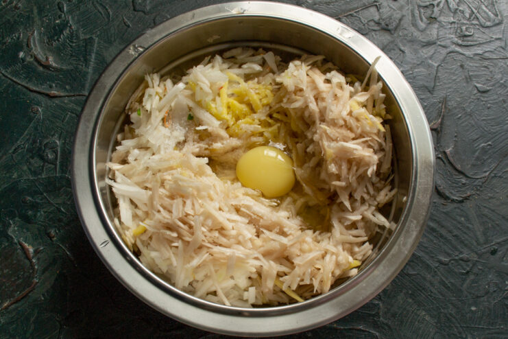 Adding eggs to the vegetable mixture. This will act as a binder for the patties. Adding two eggs to the bowl with the squeezed grated vegetables and chopped onion.