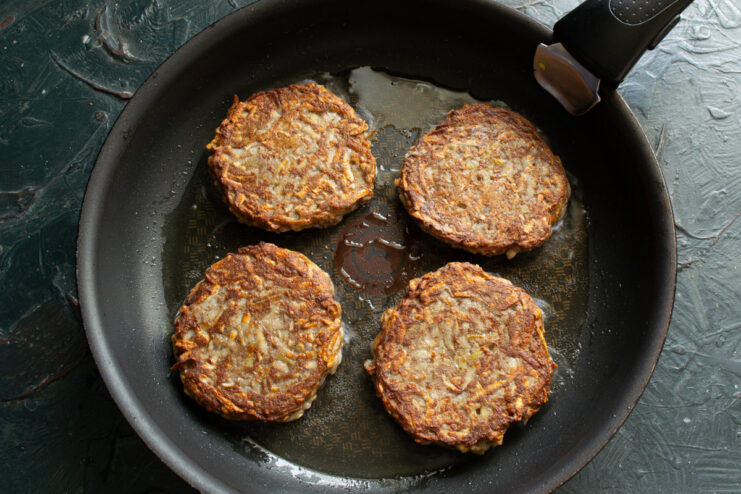 Cooking the patties slowly on low heat ensures they are cooked through and golden. Jerusalem artichoke patties frying in a pan, covered with a lid to cook through.