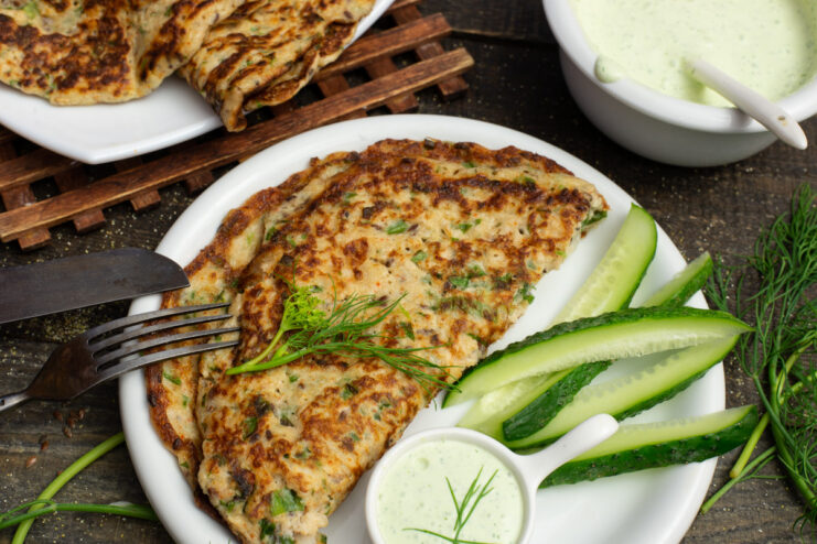 A plate with a finished Kefir Ovsyanoblin, drizzled with a creamy green sauce and garnished with fresh herbs.