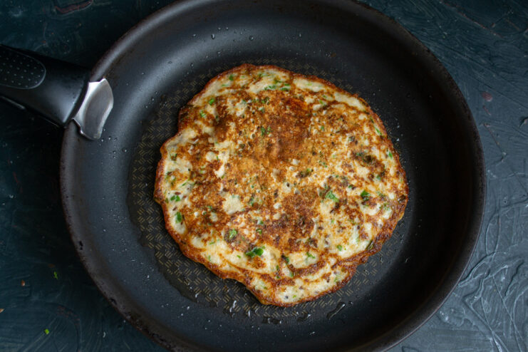 Flipping the Pancake to Cook the Other Side A golden-brown ovsyanoblin being flipped in a frying pan with a spatula.