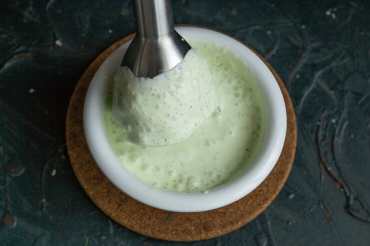 Blending the Sauce Until Smooth and Green An immersion blender mixing smetana and dill to create a smooth green sauce.