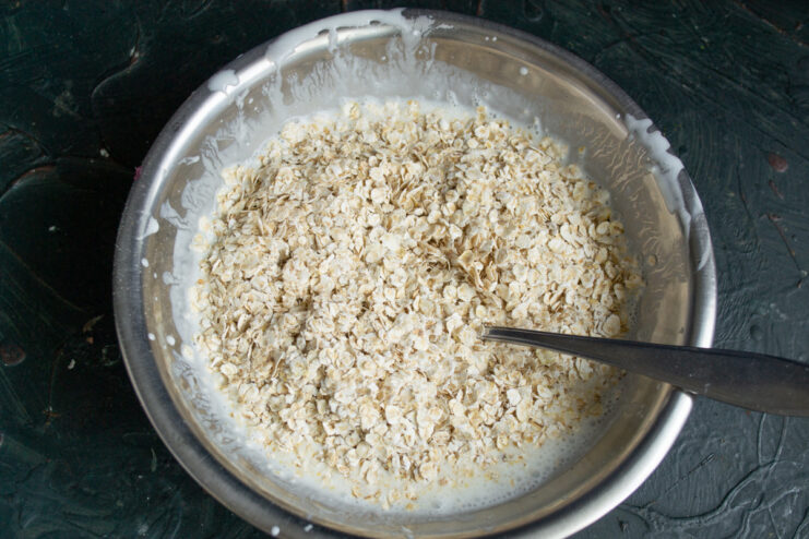 Step 2: Adding Oats to the Kefir-Egg Mixture Rolled oats being added to the whisked egg and kefir mixture in a glass bowl.