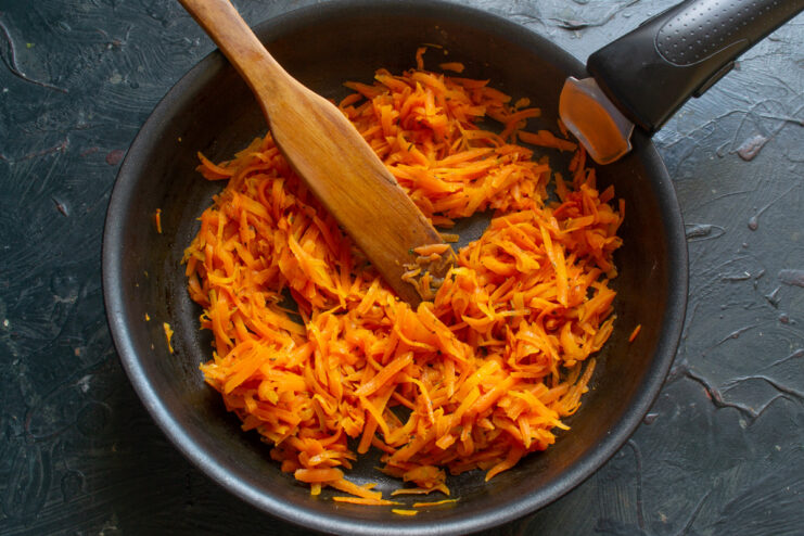 Cooking grated carrots with herbs in a frying pan Grated carrots seasoned with salt and dried thyme being stewed in a black frying pan.
