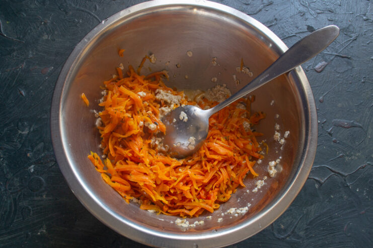 Combining stewed carrots with oats for the pancake batter Adding cooled stewed carrots to the bowl of rolled oats and whey.